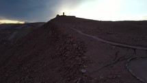 Aerial shot drone flies up red hill toward monument near Death Valley in Atacama desert at sunset