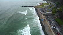Aerial shot drone descends over rocky beach next to coastal highway on cloudy day