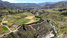 Aerial shot drone flies over multi color fields next to winding river in valley