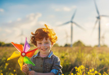 AI Generated Image. Cute redhead boy with colorful pinwheel in front of the wind turbines in summer meadow