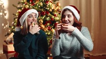 Two girls are eating the Christmas sweet Italian Panettone against the tree