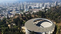 Aerial shot drone flies over round music venue and theater with city skyline in background