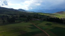 Aerial shot drone flies over valley with farms and rolling green fields covered under cloud shade