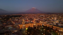 Aerial shot drone flies backwards from Plaza de Armas with Misti Volcano in distance at sunset
