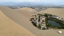 Aerial shot drone flies over ridge along inside of giant sand dune next to desert city oasis Huacachina, Peru