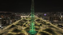 Drone facing east ascends in front of TV Tower in Brasilia, Brazil as the lights change from green to blue