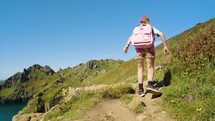 Young girl in colorful clothes walking on hiking path along beautiful coastal hills