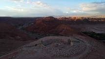 Aerial shot drone orbits viewpoint overlooking red desert mountains and green oasis in Atacama at sunset