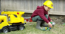 Toddler boy playing with construction worker toys outdoors in backyard - close up