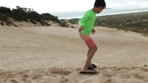 Young boy begins sandboarding down dune hill in front of beach on summer day - success at visualization