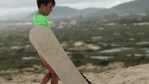 Boy carrying sand boards across dunes after riding down hill - Brazil outdoor activities