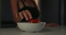 Young adult woman eating strawberries on counter in morning - close up on hand and berries