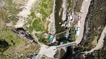 Aerial shot drone descends with camera facing down over Calera thermal baths and people walking across pedestrian bridge crossing river