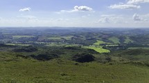 Drone flies to the left low over hiking trail with enitre sunlit valley in the background