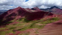 Aerial shot drone flies forward while descending on valley with red mountains and green vegetation