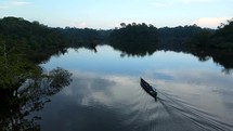Aerial shot drone follows canoe boat on black lagoon in middle of Amazon rainforest just before sunset as it enters smaller cove