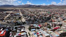 Aerial shot drone flies forward and to the left as the camera pans right over town with dirt roads