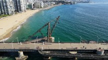 Aerial shot drone flies backwards from pier jutting out from sandy beach over green blue waters