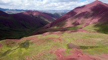 Aerial shot drone flies forward over green fields growing out of red mountains