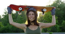 Attractive young female skateboarder in front of sunset turns away from camera to look at sunset - lens flare
