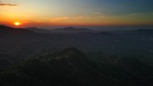 Aerial shot drone panning right over mountains facing the sunset in the distance.