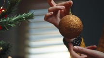 Girl rolling a golden Christmas ball during decoration near the tree