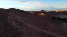Aerial shot drone flies forward along path ascending hill in red desert at sunset