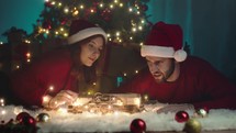 Couple are playing with train toy on the carpet against the Christmas tree