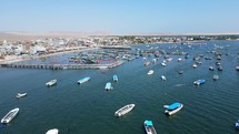 Aerial shot drone flies to the left over boat marina with wooden pier in Paracas, Peru