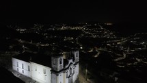 Drone flies over Church of Santa Efigenia at night toward historic center of Ouro Preto