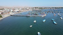 Aerial shot drone flies forward over boat marina with wooden pier in Paracas, Peru