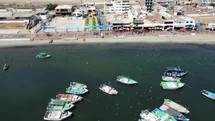 Aerial shot drone flies backwards from beach and seabirds eating over boats in marina