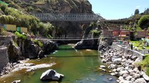 Aerial shot drone flies low over river toward wooden bridge at Calera thermal baths