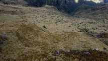 Aerial shot drone flies backwards with camera pointing down at 75 degree angle as it flies over mountain trail and two hikers passing by