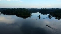 Aerial shot drone flies forward over canoe boat on black lagoon in middle of Amazon rainforest just before sunset