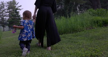 Mother holds toddler girl as they walk with older brother towards lake - cottage fun