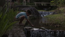 Young boy puts paper boat in water just before water fall - young imagination and play