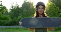 Attractive young female skateboarder pushes board towards camera with sunset behind her