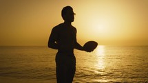 Silhouette of a boy playing with the american football ball on the beach