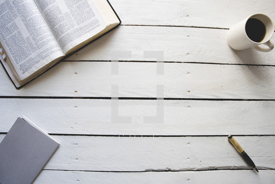 opened Bible, journal, pen, coffee cup on a white wood background 