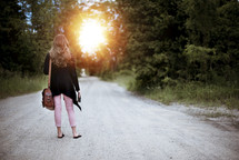 a woman standing in the middle of a dirt road carrying a Bible 