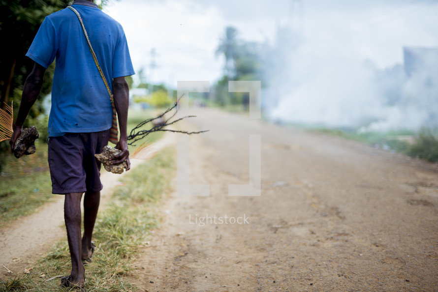 A man carrying palm bulbs on a dirt road 