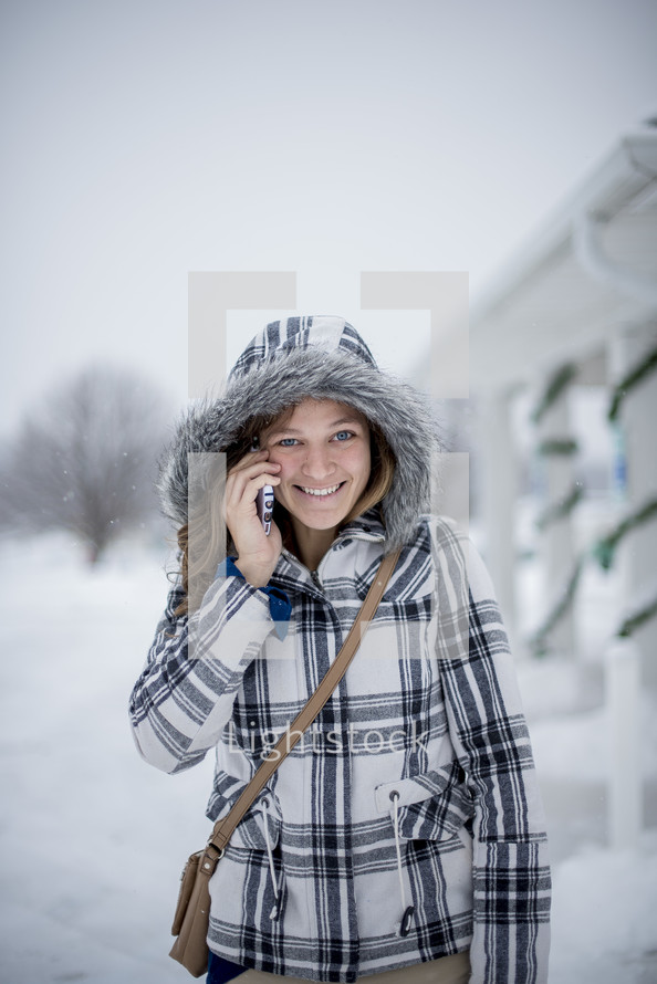 a woman in a coat talking on a cellphone in the snow 