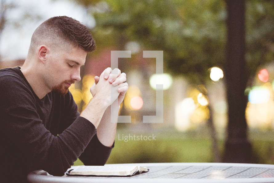 man praying with head bowed reading a Bible 