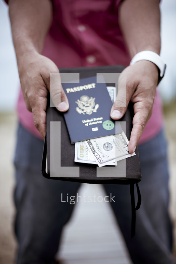 man holding a passport, cash, and Bible 