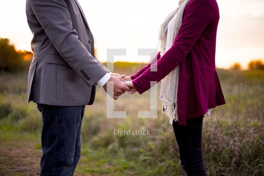 couple standing outdoors in a field holding hands 