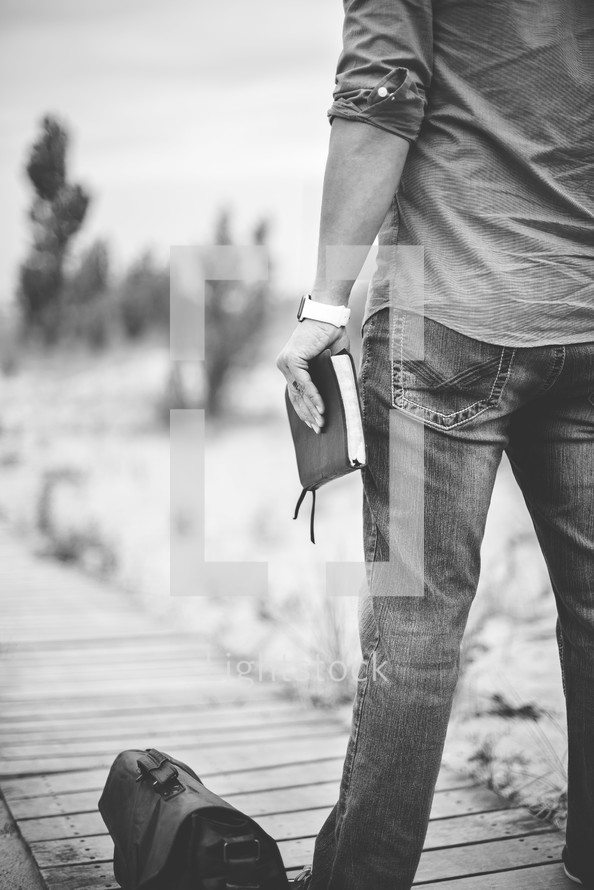 man holding a Bible standing on a boardwalk 