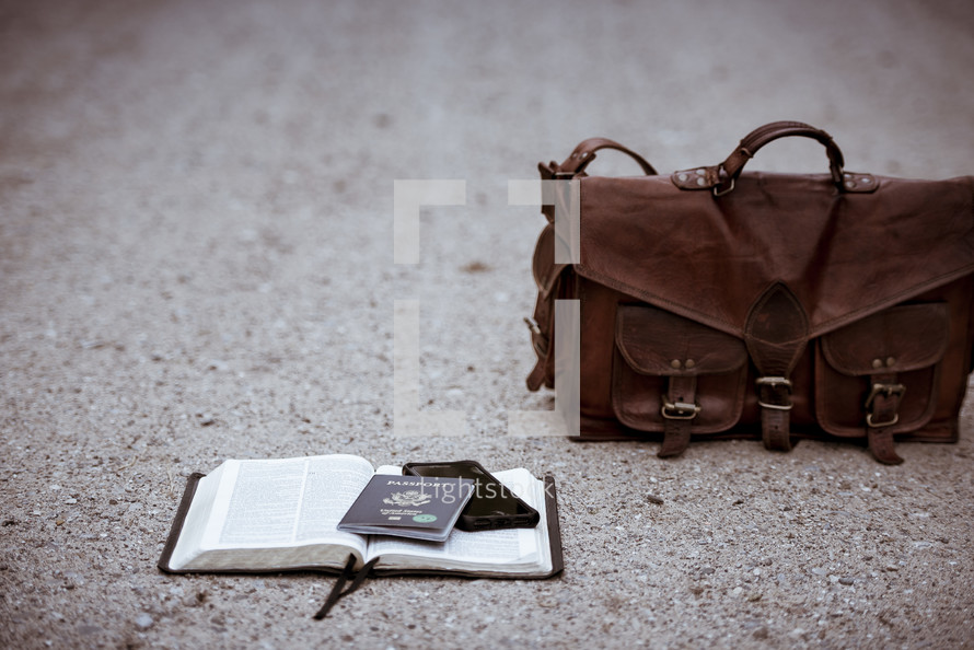passport and phone on an opened Bible on a gravel road 