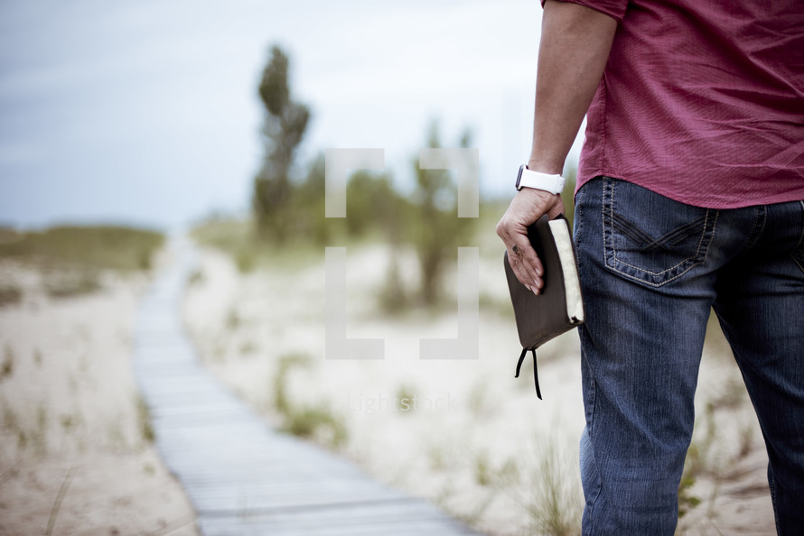 a man holding a Bible walking on a boardwalk 