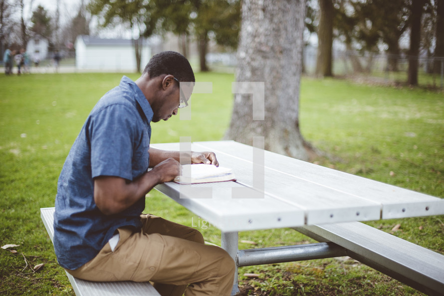 a man reading a Bible at a picnic table 